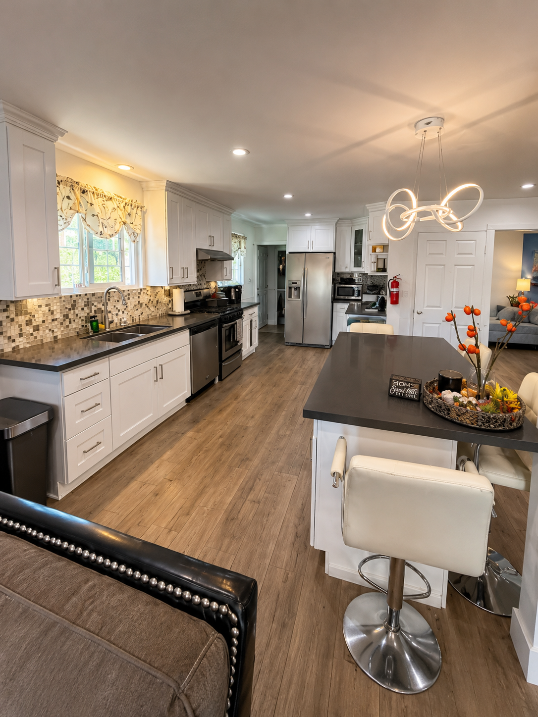 Bright kitchen with white cabinetry, dark countertops and a central island with bar stools